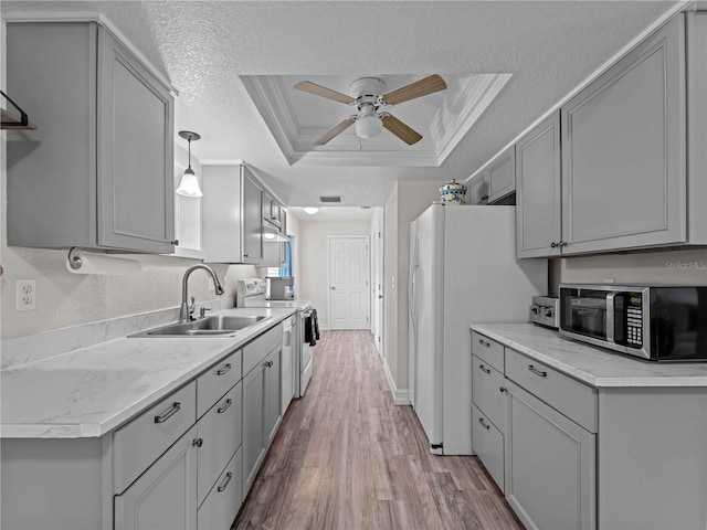 kitchen featuring gray cabinets, a tray ceiling, white appliances, and sink