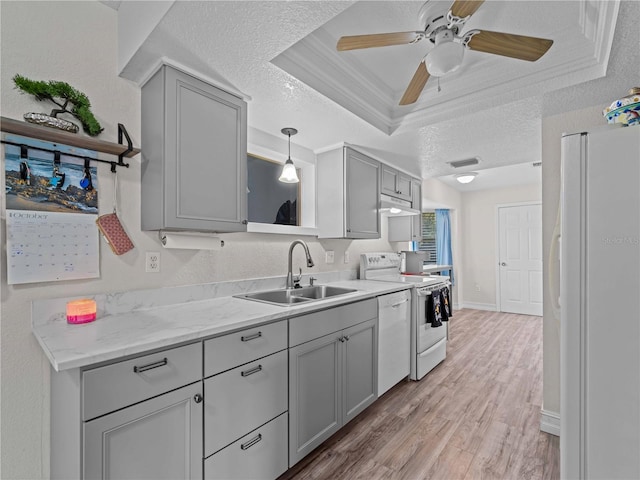 kitchen with light hardwood / wood-style floors, white appliances, a tray ceiling, sink, and a textured ceiling