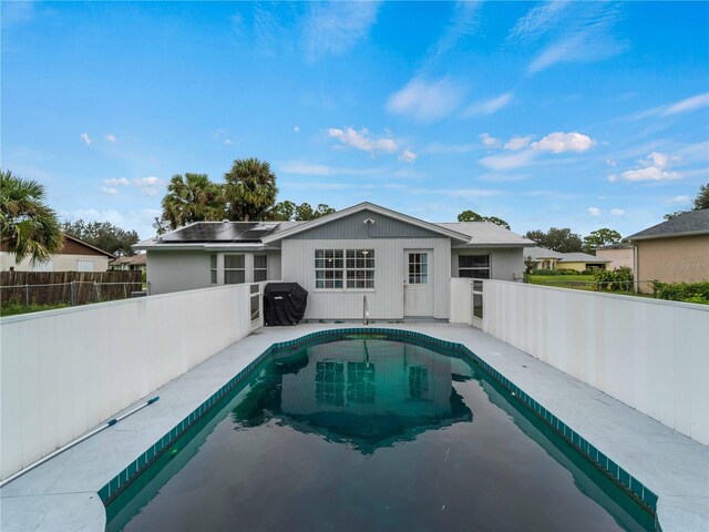 back of property with a fenced in pool and solar panels