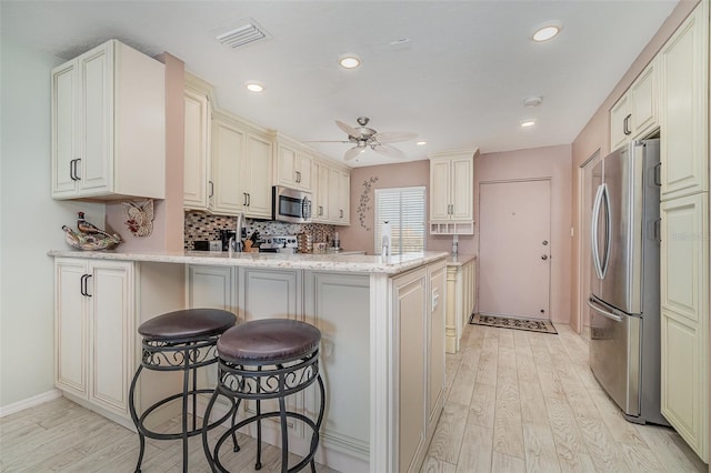 kitchen featuring kitchen peninsula, stainless steel appliances, light stone countertops, light wood-type flooring, and ceiling fan