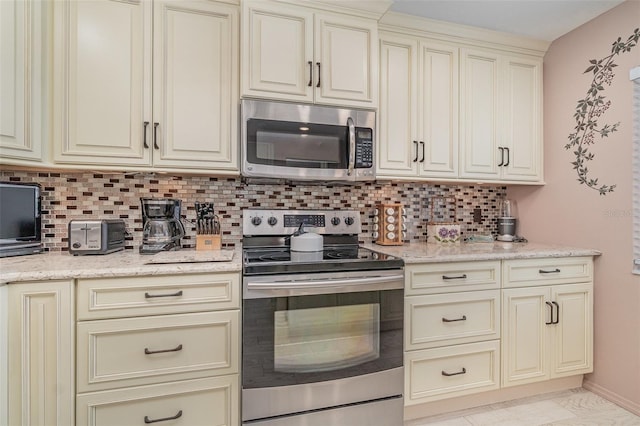 kitchen featuring backsplash, light stone countertops, light tile patterned flooring, cream cabinetry, and stainless steel appliances