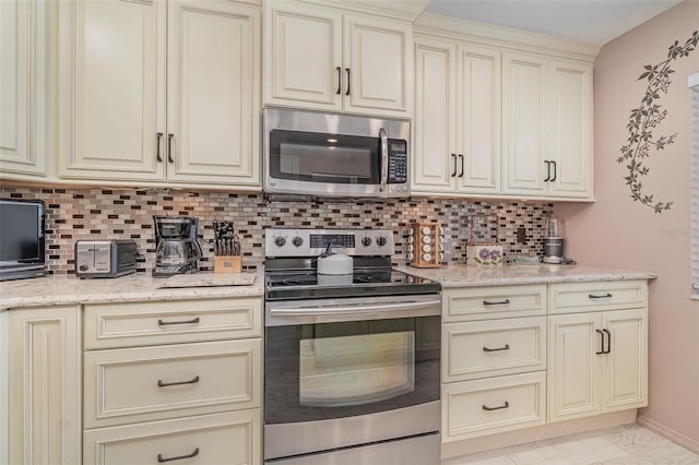 9011 Midnight Pass Rd Unit 329, Sarasota, FL 34242 - kitchen featuring appliances with stainless steel finishes, cream cabinets, decorative backsplash, and light stone countertops