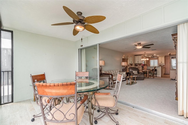 dining space with a textured ceiling, ceiling fan with notable chandelier, and light hardwood / wood-style floors