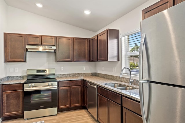 kitchen with appliances with stainless steel finishes, sink, light wood-type flooring, vaulted ceiling, and light stone counters