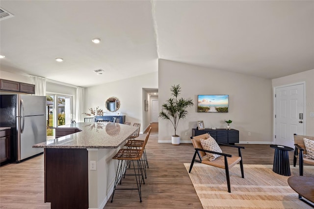 kitchen with lofted ceiling, stainless steel fridge, dark brown cabinetry, and light wood-type flooring