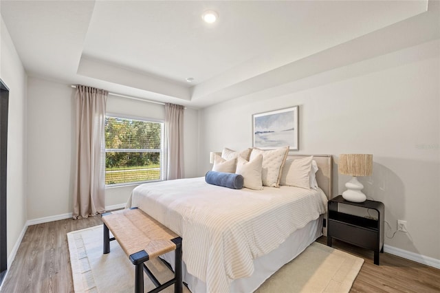 bedroom with a tray ceiling and light hardwood / wood-style flooring