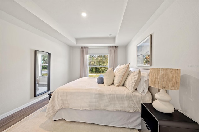 bedroom with a tray ceiling, wood-type flooring, and multiple windows