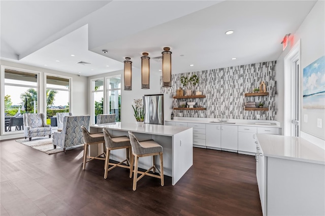 kitchen featuring stainless steel refrigerator, white cabinetry, backsplash, a breakfast bar area, and a kitchen island