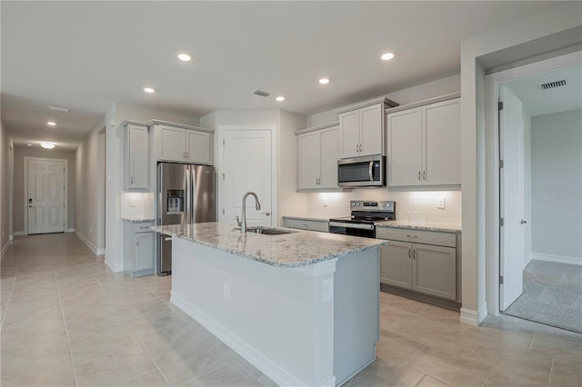 kitchen with light stone countertops, sink, a kitchen island with sink, stainless steel appliances, and decorative backsplash