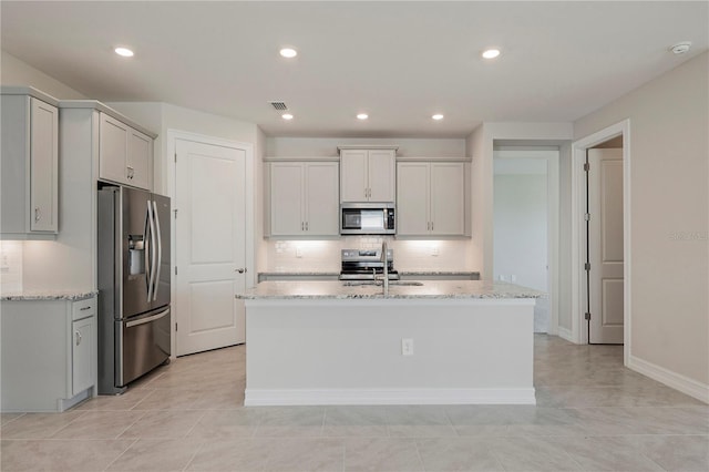 kitchen featuring light stone countertops, an island with sink, stainless steel appliances, and sink