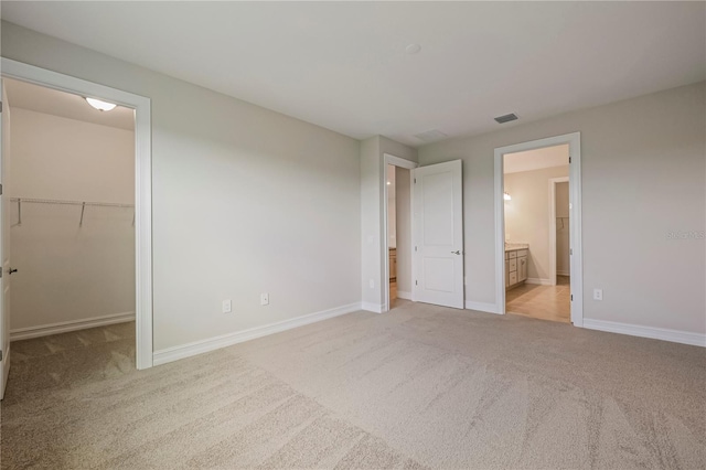 unfurnished bedroom featuring connected bathroom, light colored carpet, a spacious closet, and a closet