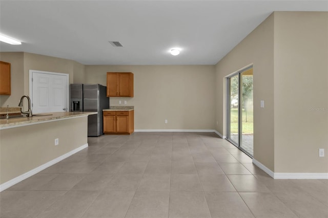 kitchen featuring stainless steel refrigerator with ice dispenser, light stone countertops, sink, and light tile patterned floors