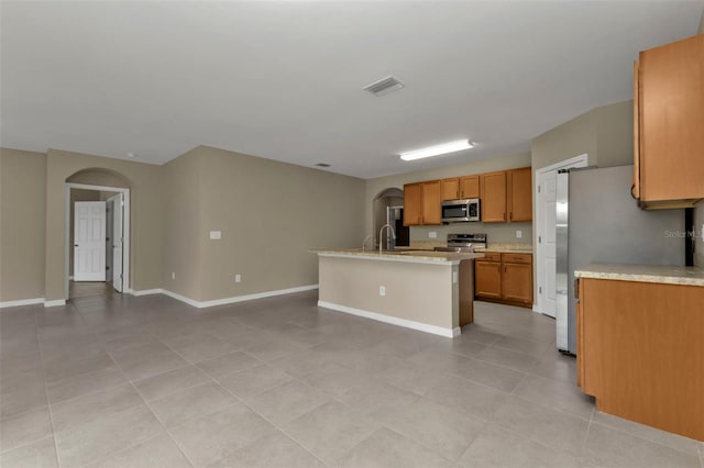 kitchen featuring appliances with stainless steel finishes, sink, light tile patterned floors, and an island with sink