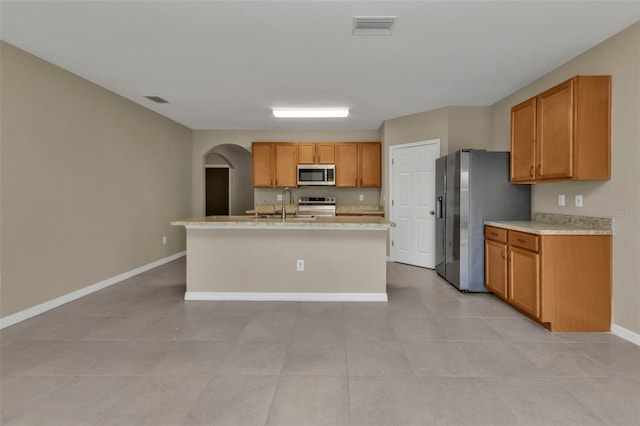 kitchen with appliances with stainless steel finishes, sink, a center island with sink, and light tile patterned floors