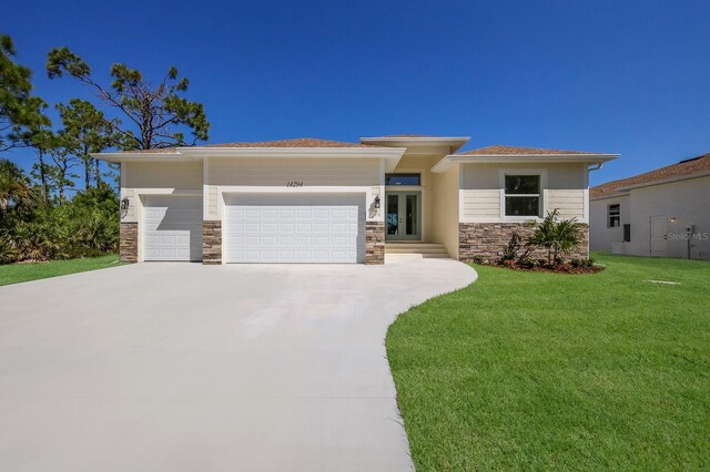 14294 Mcfarland Ave, Port Charlotte, FL 33981 - prairie-style house featuring a garage, stone siding, french doors, a front lawn, and concrete driveway