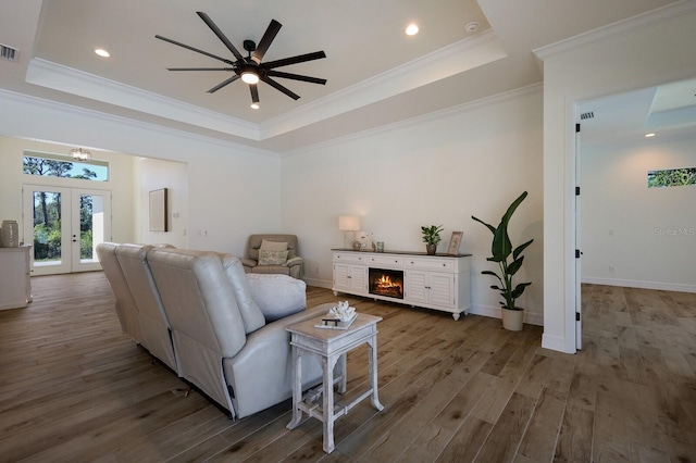 living room with french doors, a raised ceiling, hardwood / wood-style floors, ceiling fan, and crown molding