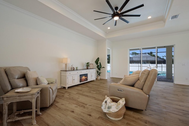 living room with crown molding, a tray ceiling, light wood-type flooring, and ceiling fan