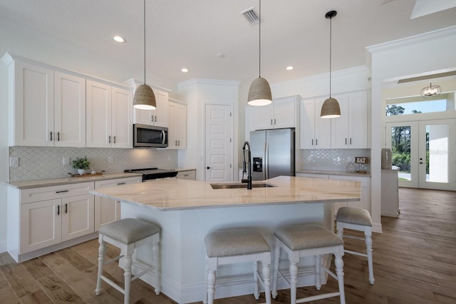 kitchen featuring appliances with stainless steel finishes, white cabinetry, decorative light fixtures, and a center island with sink