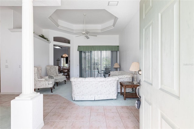 tiled living room featuring a tray ceiling, ceiling fan, and ornate columns