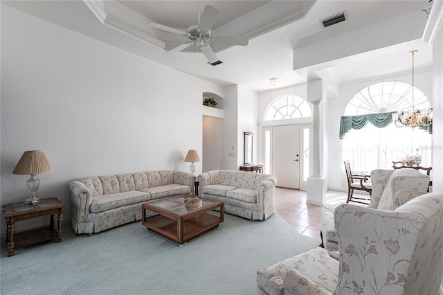 tiled living room with a towering ceiling, a raised ceiling, ceiling fan with notable chandelier, and ornate columns