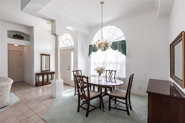 tiled dining space featuring ornamental molding, decorative columns, a chandelier, and a high ceiling