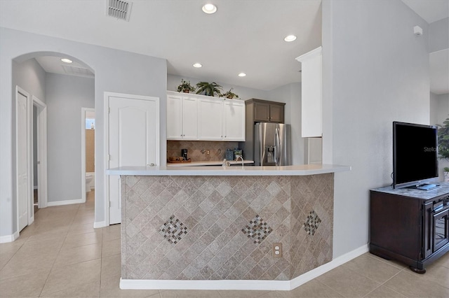 kitchen with kitchen peninsula, stainless steel fridge, backsplash, light tile patterned floors, and white cabinetry