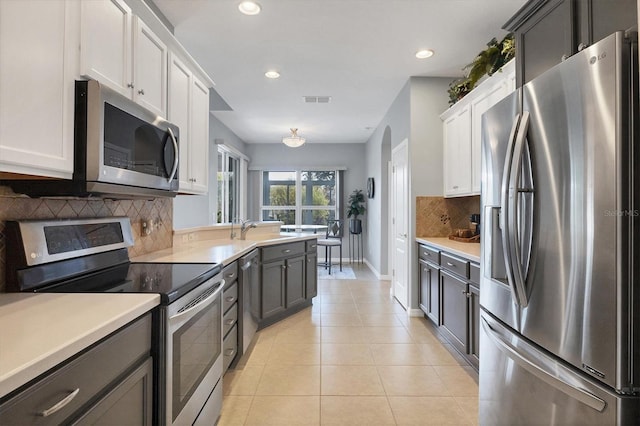 kitchen with appliances with stainless steel finishes, light tile patterned flooring, sink, backsplash, and white cabinets