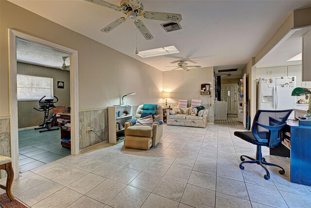 tiled living room with ceiling fan and wood walls