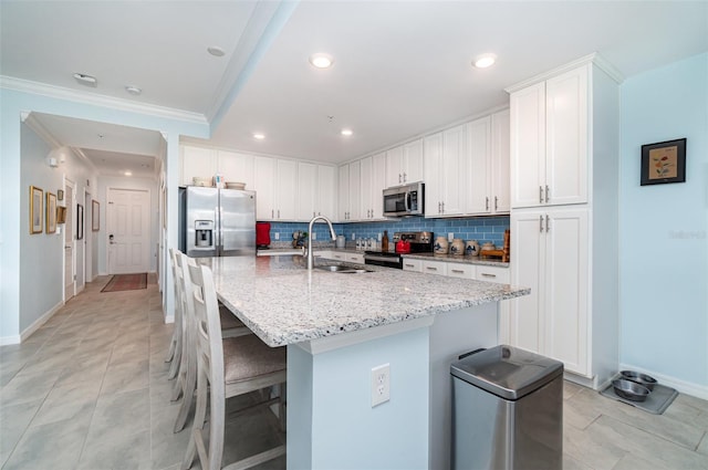 kitchen with crown molding, white cabinets, stainless steel appliances, and an island with sink