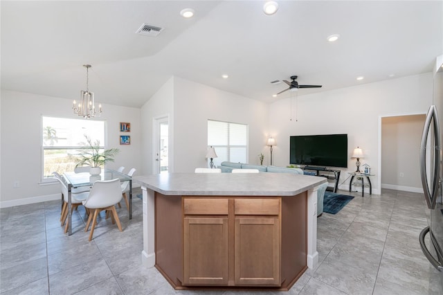 kitchen with stainless steel refrigerator, vaulted ceiling, ceiling fan with notable chandelier, pendant lighting, and a center island