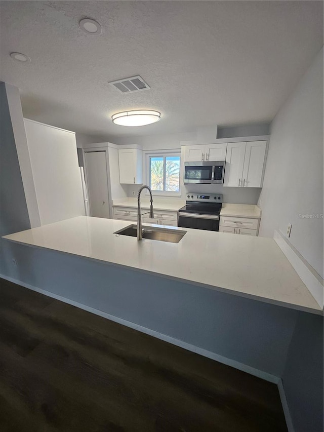 kitchen with appliances with stainless steel finishes, sink, kitchen peninsula, white cabinetry, and dark hardwood / wood-style floors