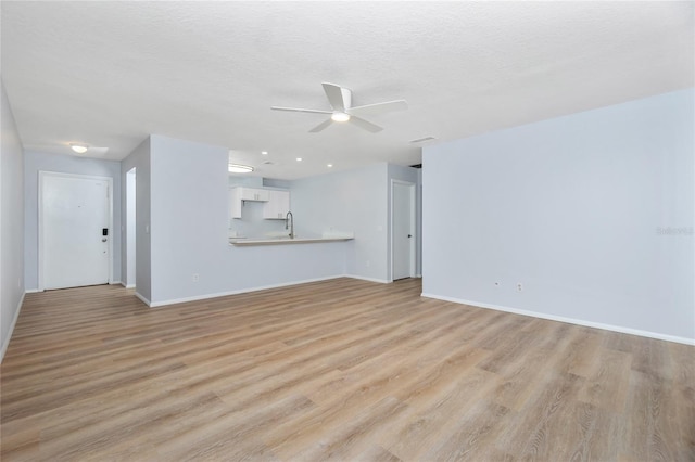 unfurnished living room with light hardwood / wood-style floors, a textured ceiling, sink, and ceiling fan