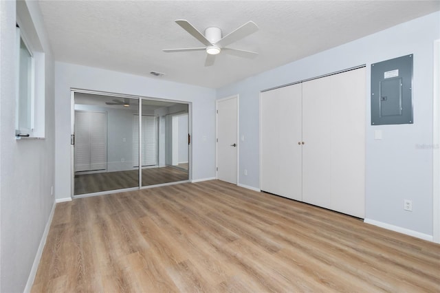 unfurnished bedroom featuring electric panel, two closets, ceiling fan, a textured ceiling, and light hardwood / wood-style flooring