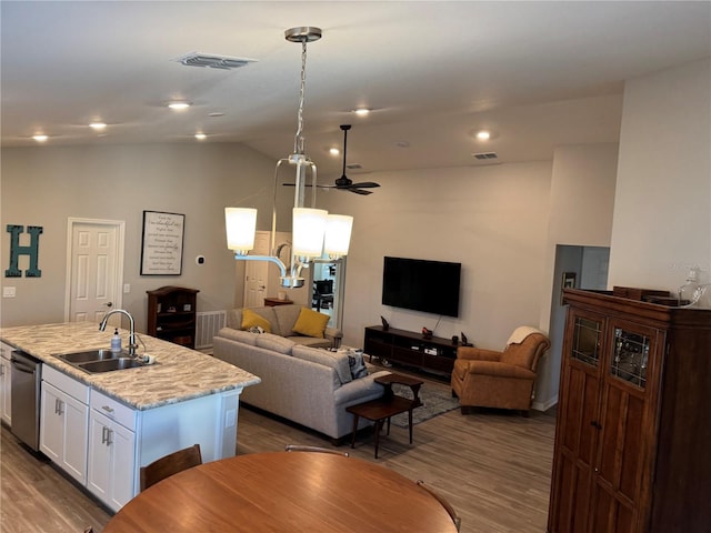 kitchen featuring white cabinetry, sink, hanging light fixtures, light stone counters, and a kitchen island with sink