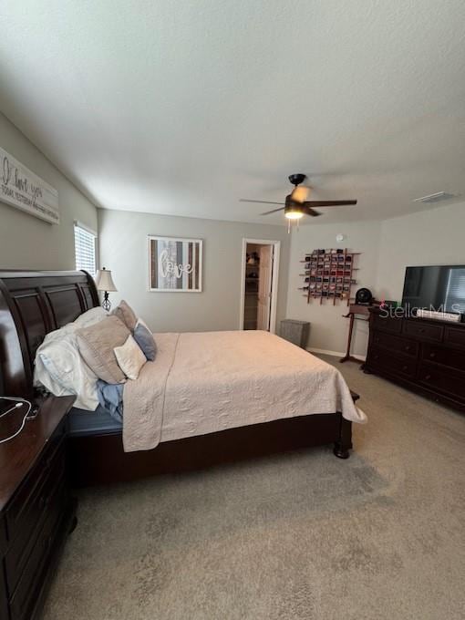 carpeted bedroom with a walk in closet, ceiling fan, a closet, and a textured ceiling