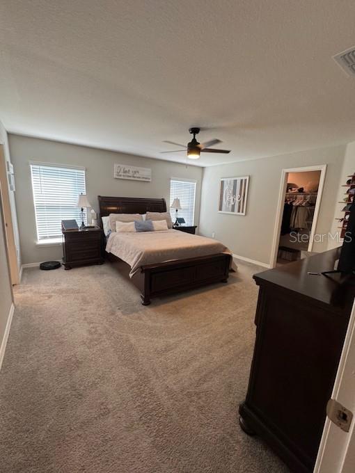 bedroom with ceiling fan, carpet flooring, a textured ceiling, and a spacious closet