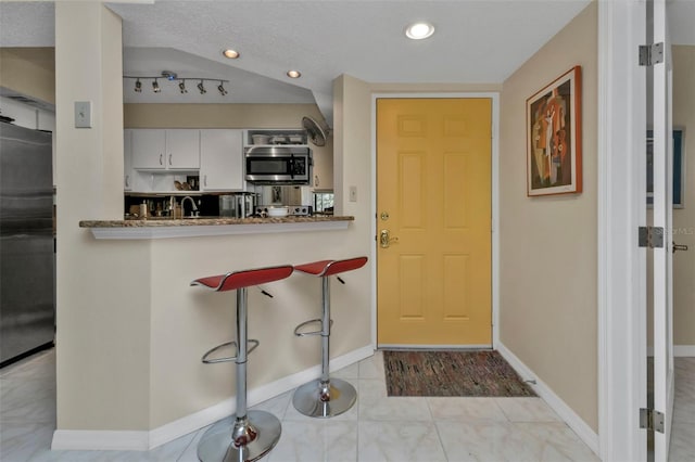 kitchen featuring appliances with stainless steel finishes, white cabinets, dark stone countertops, and a textured ceiling