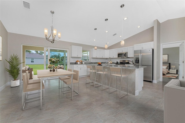 kitchen featuring a breakfast bar area, stainless steel appliances, a center island with sink, white cabinets, and high vaulted ceiling