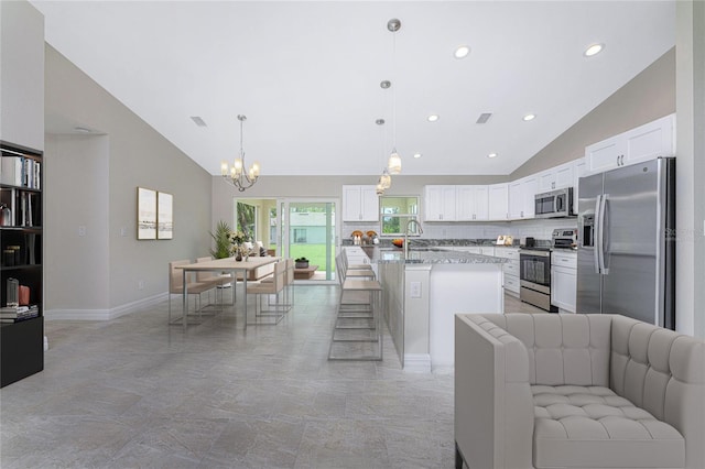 kitchen with light stone countertops, a kitchen island, hanging light fixtures, stainless steel appliances, and white cabinets