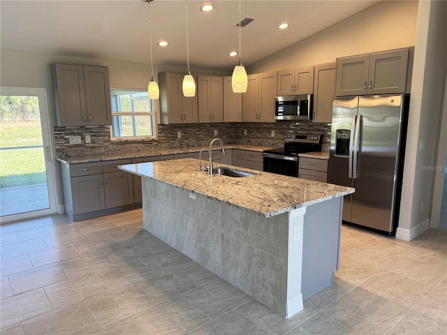 kitchen featuring light stone countertops, sink, stainless steel appliances, vaulted ceiling, and a kitchen island with sink