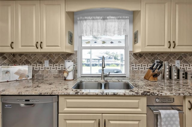 kitchen with sink, dishwasher, cream cabinetry, light stone counters, and decorative backsplash