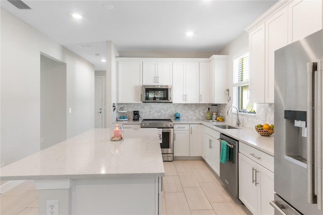 kitchen with light stone countertops, appliances with stainless steel finishes, sink, white cabinets, and a kitchen island