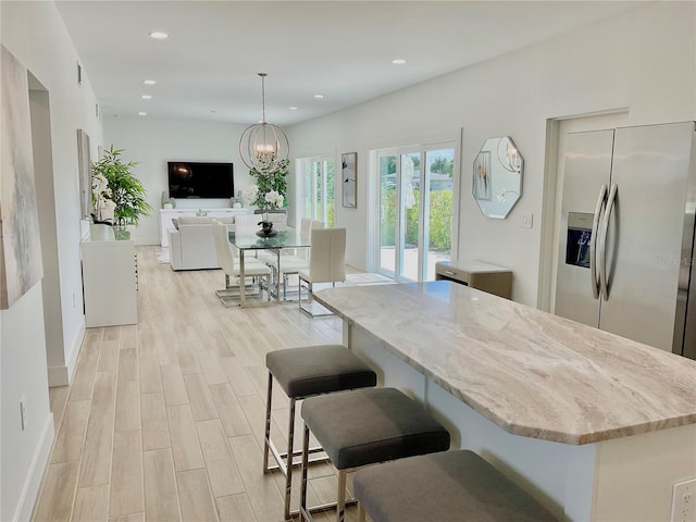 kitchen featuring stainless steel refrigerator with ice dispenser, a chandelier, light hardwood / wood-style flooring, a kitchen island, and pendant lighting