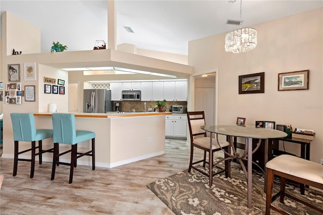 kitchen featuring white cabinets, appliances with stainless steel finishes, a kitchen breakfast bar, light hardwood / wood-style flooring, and a towering ceiling