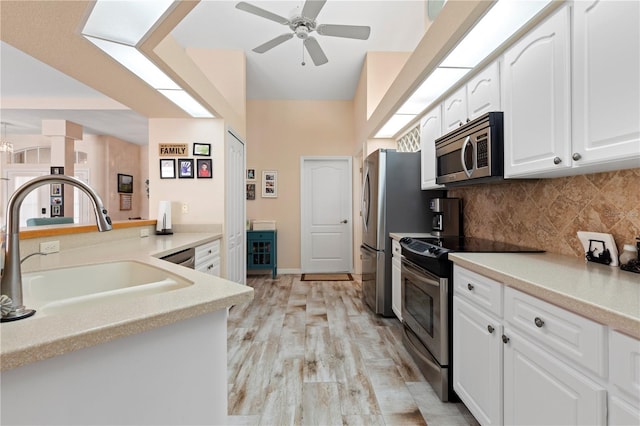 kitchen with kitchen peninsula, white cabinets, light wood-type flooring, sink, and stainless steel appliances