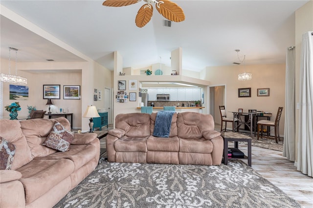 living room with lofted ceiling, ceiling fan with notable chandelier, and light wood-type flooring