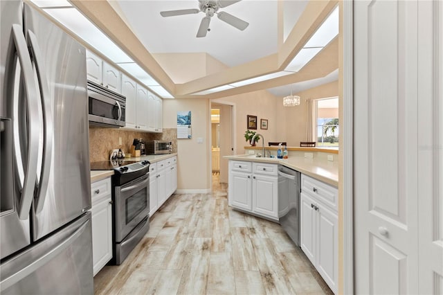 kitchen with white cabinetry, hanging light fixtures, stainless steel appliances, and light hardwood / wood-style floors