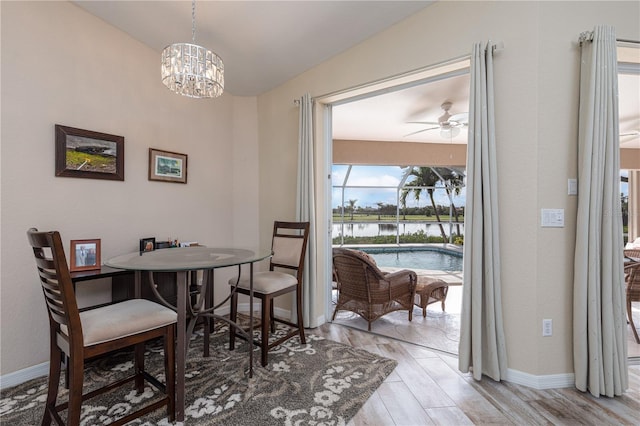 dining room with ceiling fan with notable chandelier, a water view, and light wood-type flooring