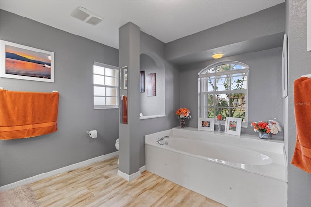 bathroom with toilet, plenty of natural light, hardwood / wood-style floors, and a bath