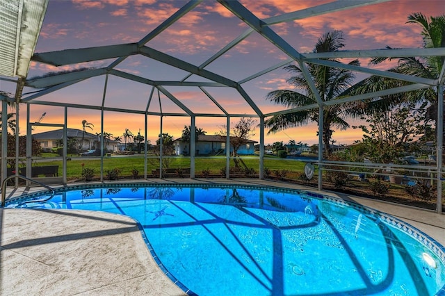 pool at dusk featuring a patio, glass enclosure, and a lawn